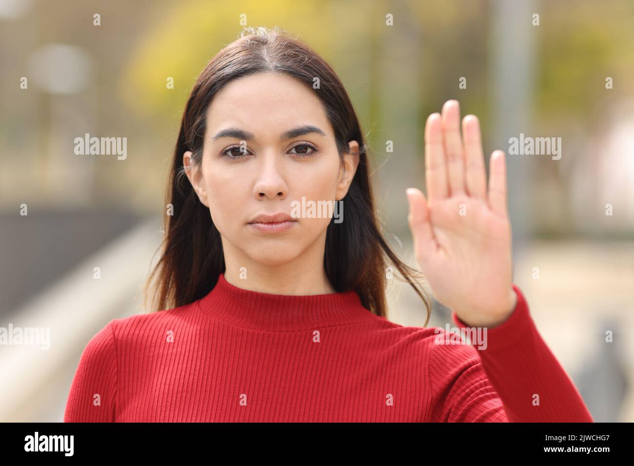 Front view portrait of a serious woman in red gesturing stop with hand in the street Stock Photo