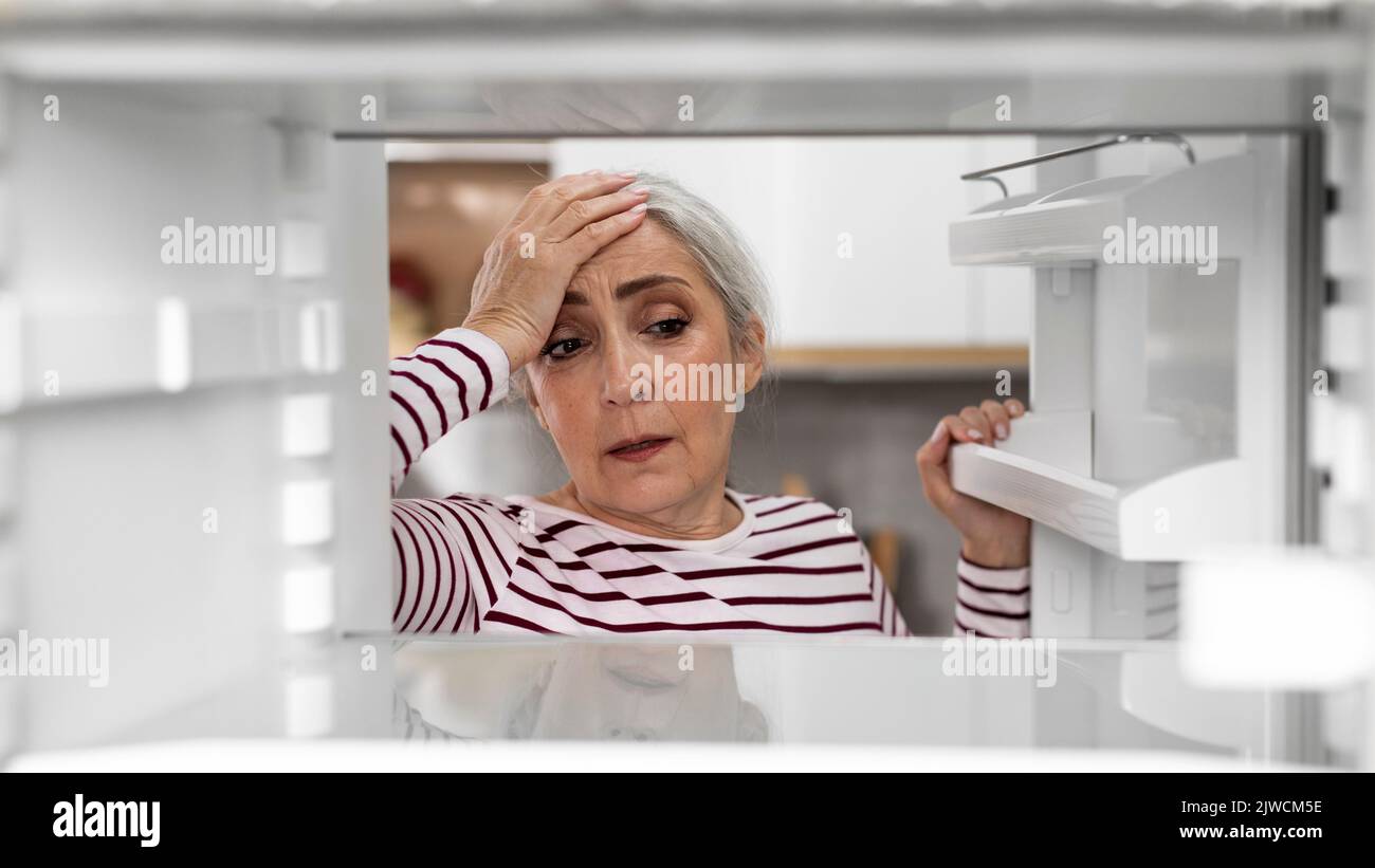 Hungry Senior Woman Looking Inside Of Fridge With No Food Stock Photo