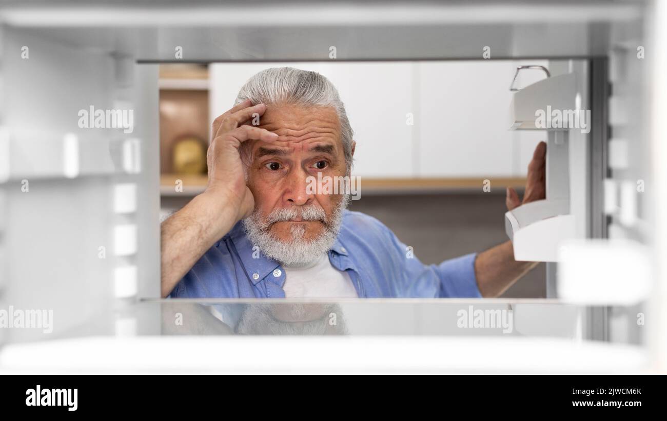 Portrait Of Hungry Elderly Man Searching For Food In Empty Fridge Stock Photo