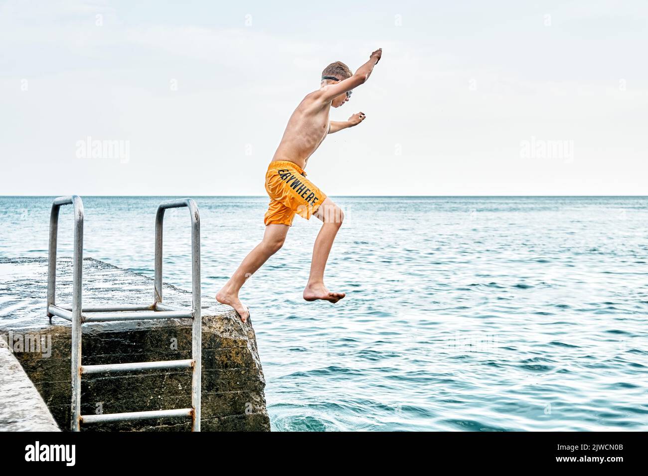 Moments of schoolboy jumping from stone pier with ladder into sea doing tricks in combined image sequence Stock Photo