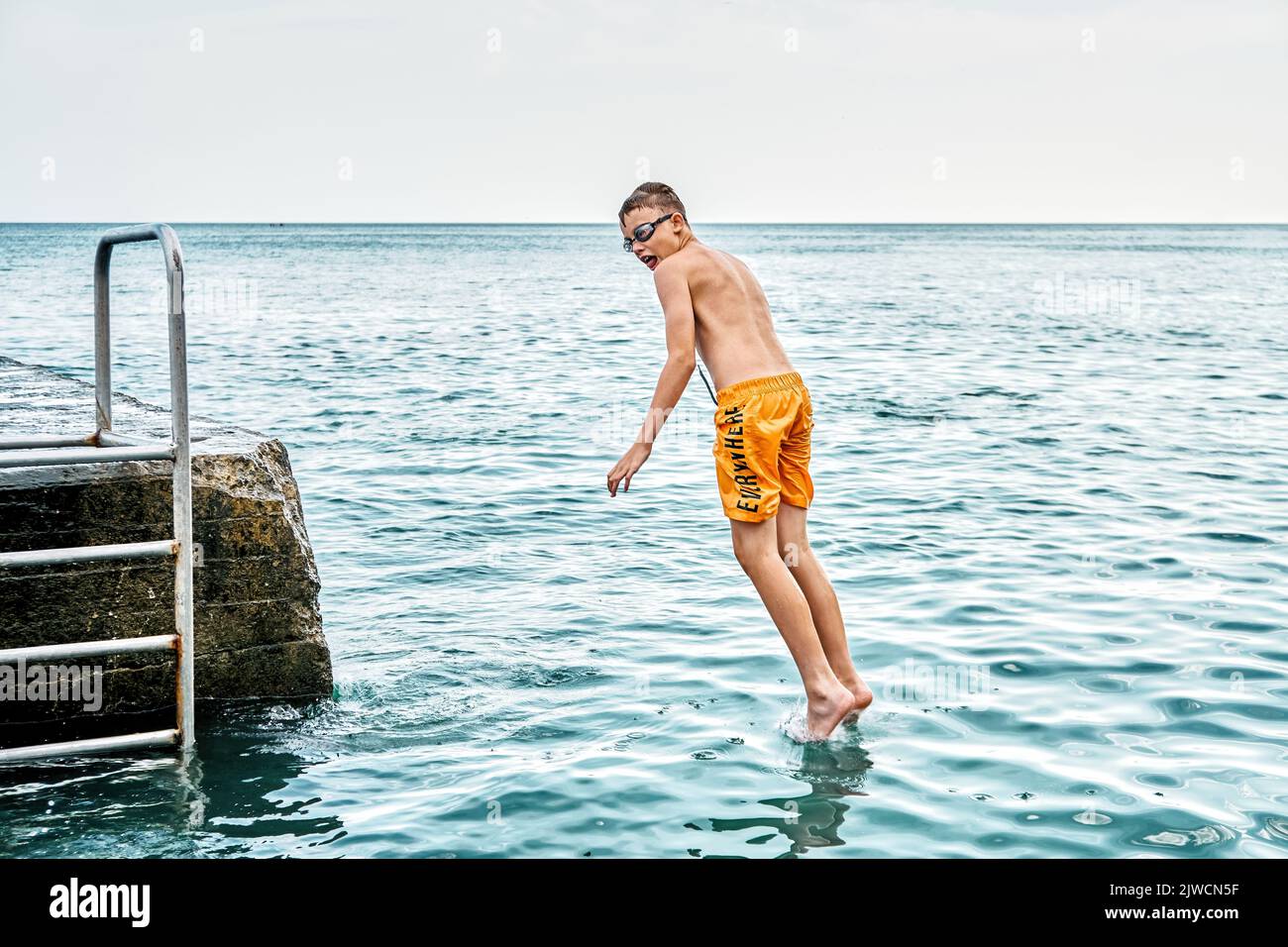 Moments of schoolboy jumping from stone pier with ladder into sea doing tricks in combined image sequence Stock Photo