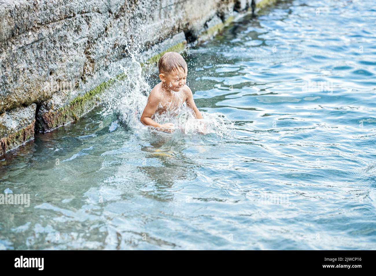 Moment of small boy diving into water while jumping in sea from pier. Small kid jumps and splashes water at summertime. Boy enjoys swimming Stock Photo