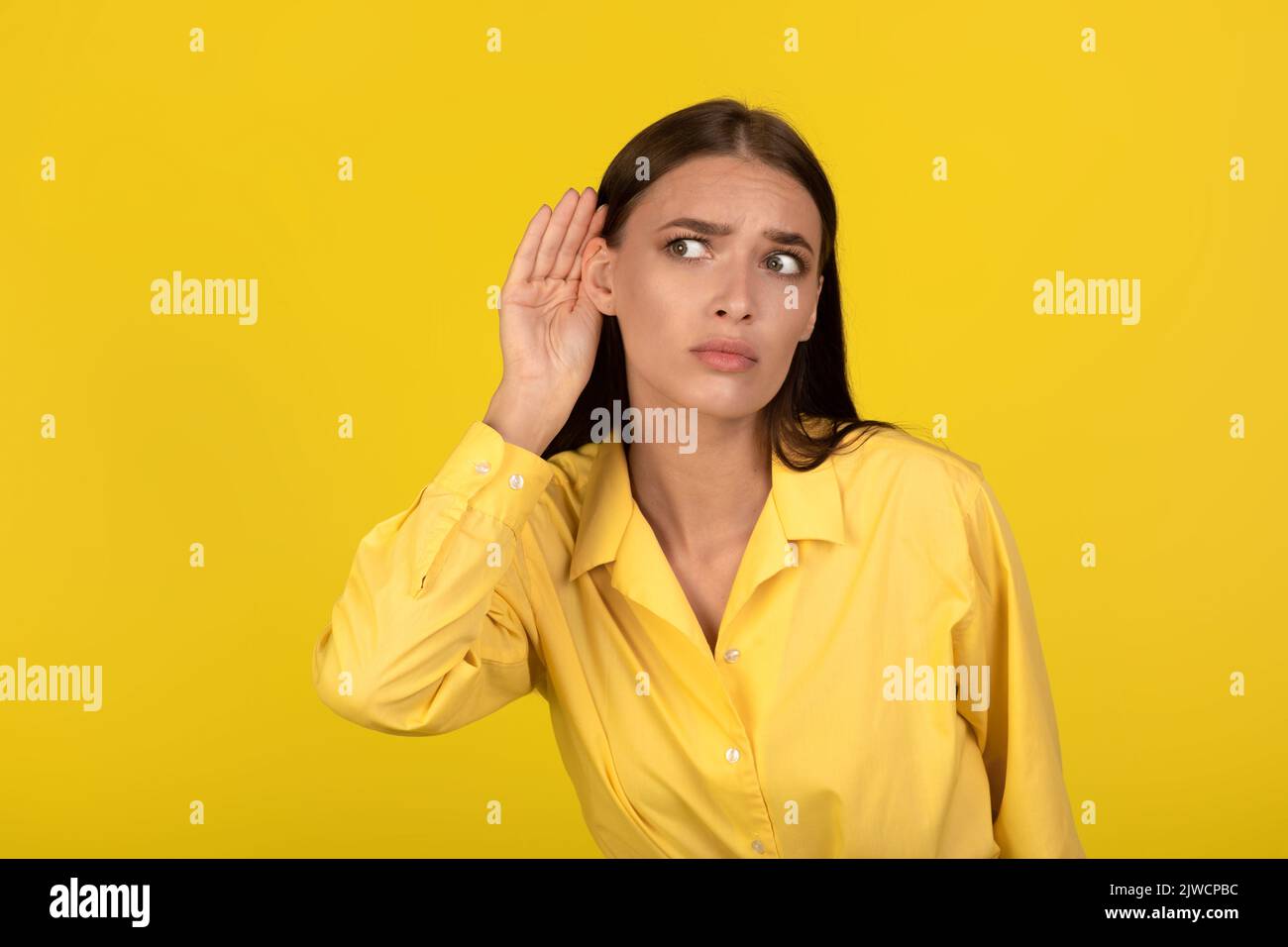 Concerned Female Eavesdropping Holding Hand Near Ear Over Yellow Background Stock Photo