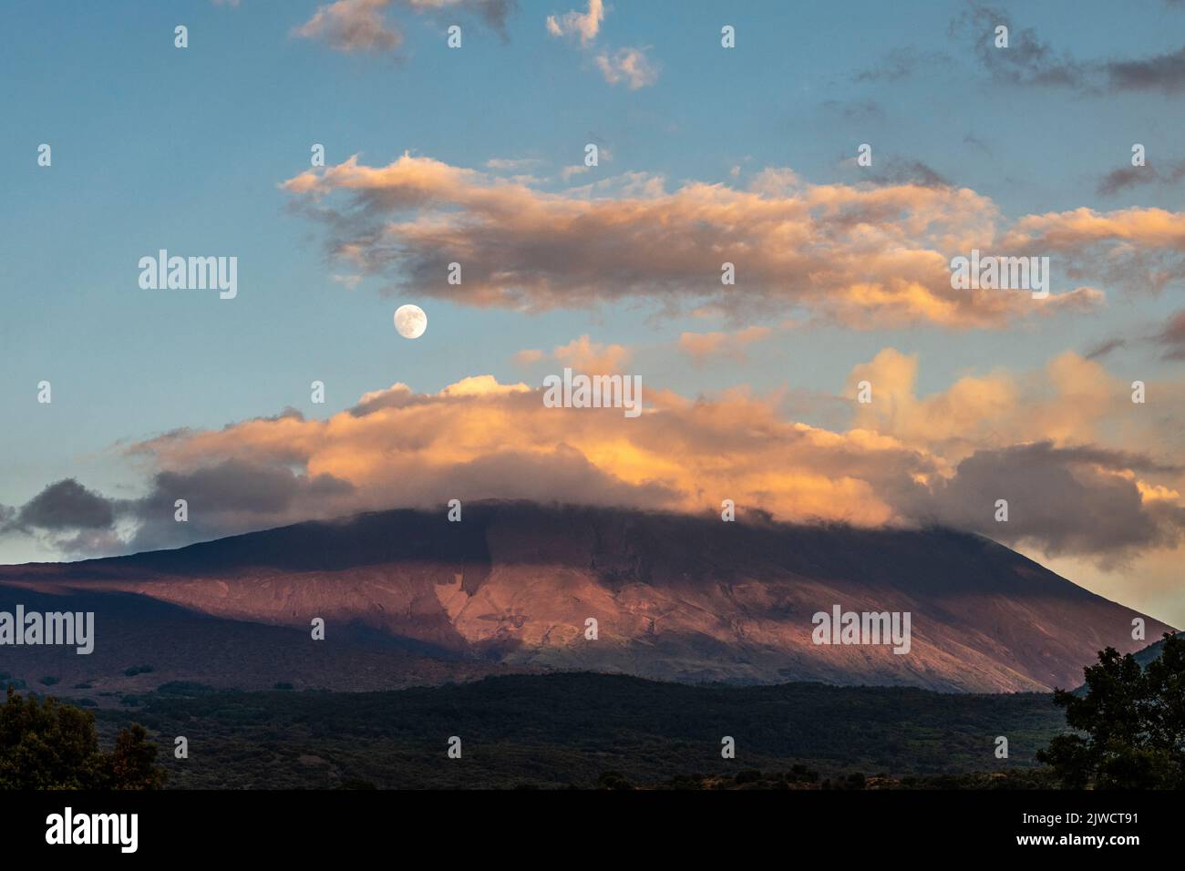 A full moon rising above Mount Etna, seen at sunset from the western side of the volcano Stock Photo