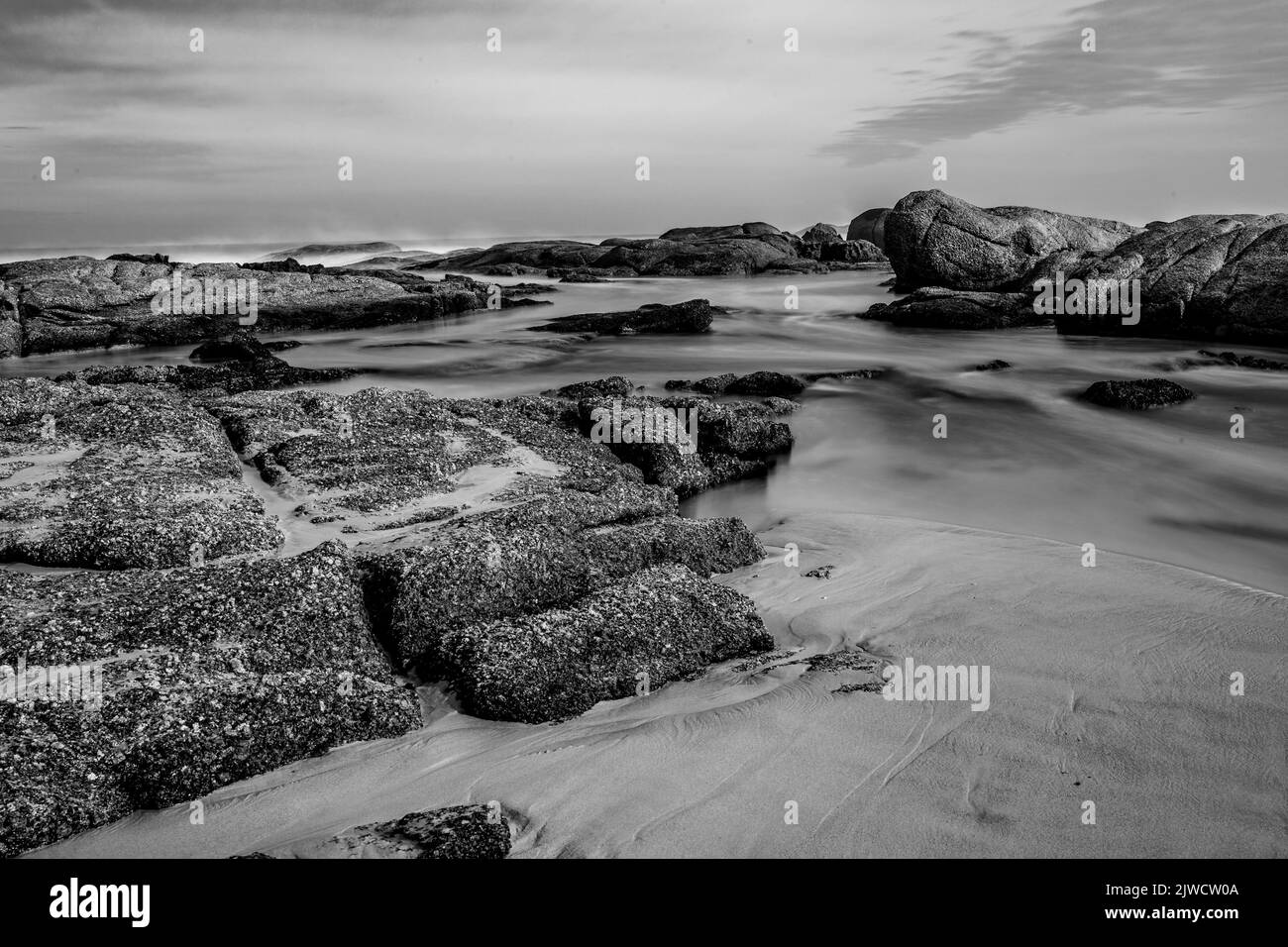 A long exposure grayscale of a rocky shore in Cape Town, at Camps Bay ...
