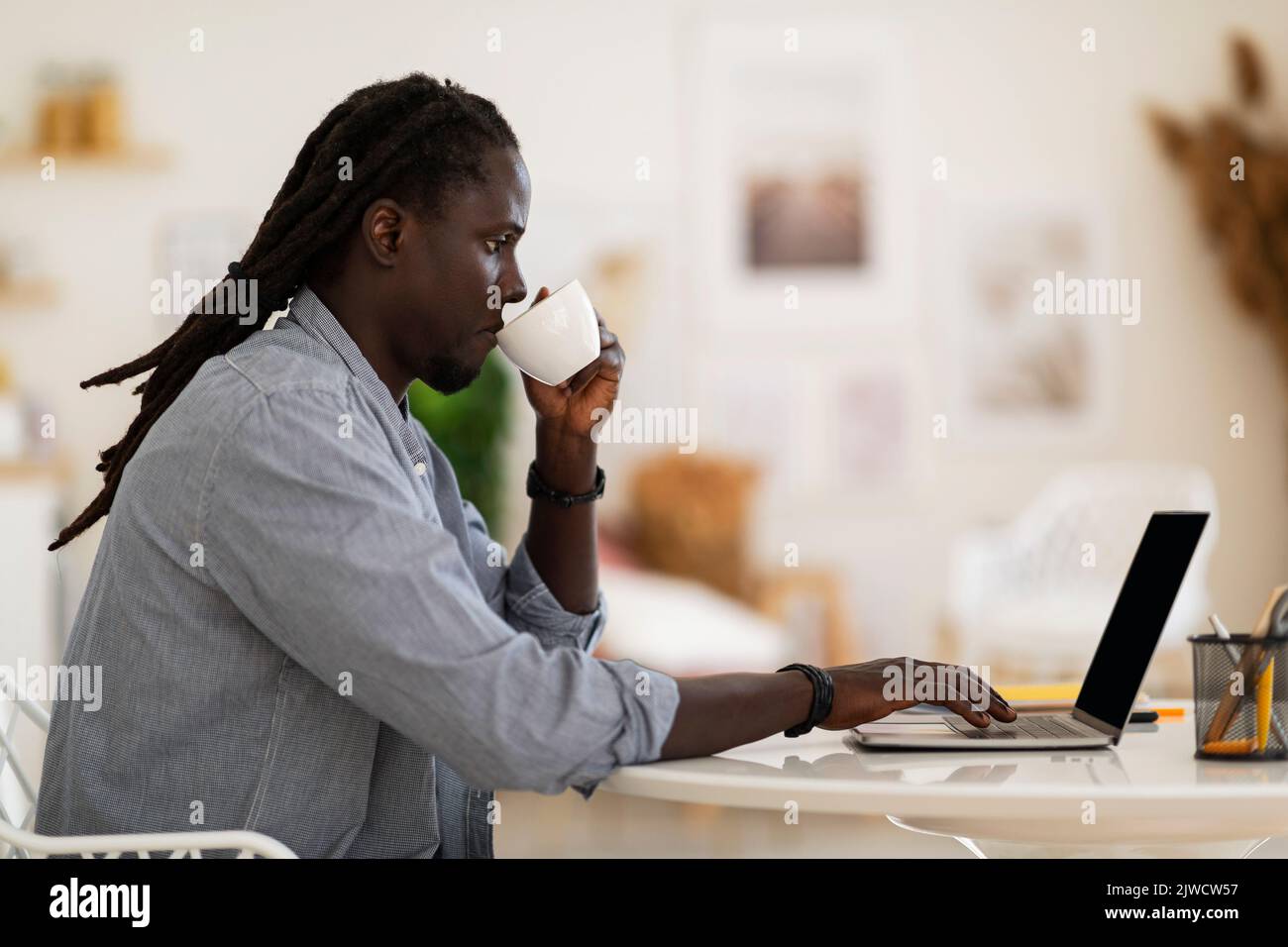 Remote Work. Black Freelancer Guy Working With Laptop And Drinking Coffee Stock Photo