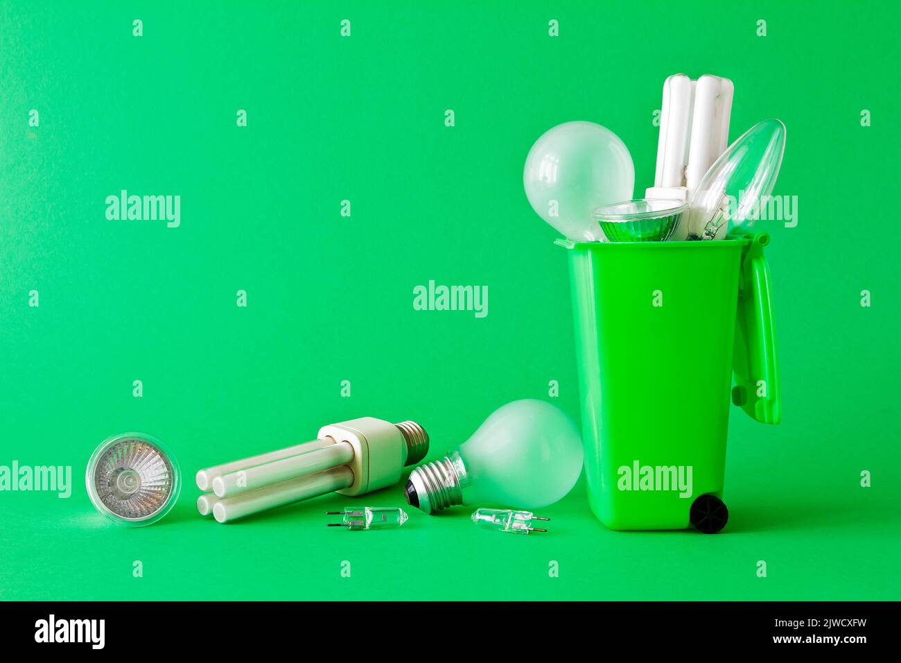 Stop energy waste concept: diverse old halogen and fluorescent light bulbs in and around a recycling bin, green background, text or copy space. Stock Photo