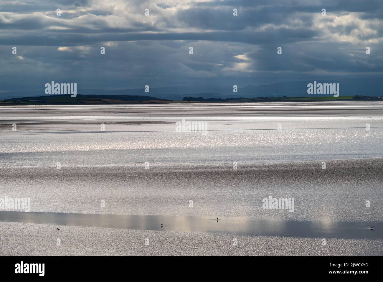 Moody landscape with dark clouds, dark sky and sunlight reflecting off the sea. View across Morecambe Bay from Canal Foot, Ulverston, Cumbria, UK Stock Photo