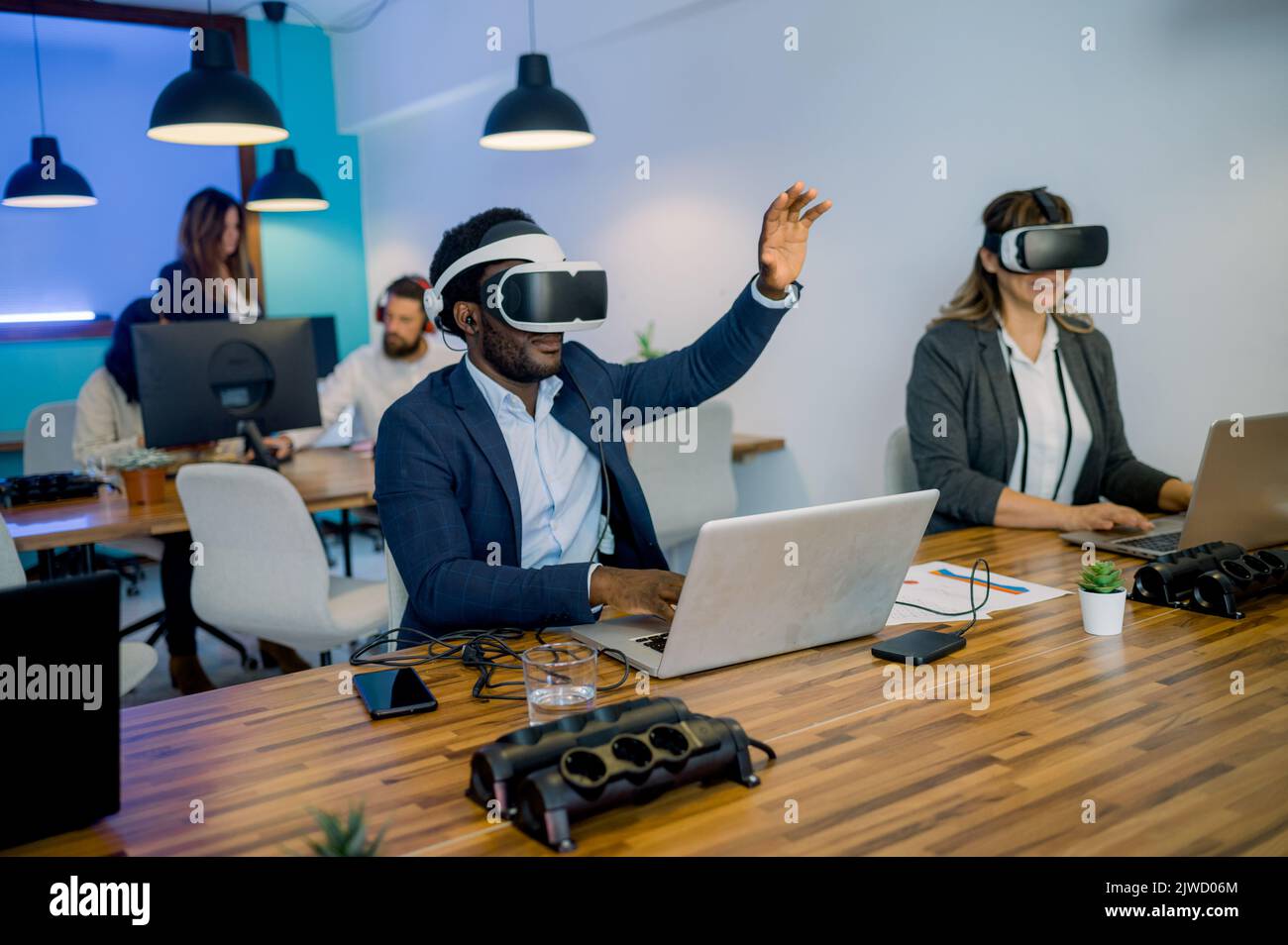 Multiracial colleagues in VR glasses using laptops in modern coworking space Stock Photo