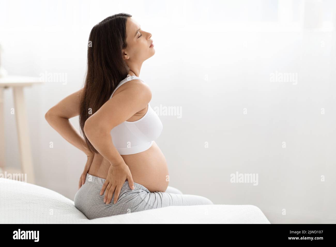 Pregnant woman having back pain, sitting on bed Stock Photo