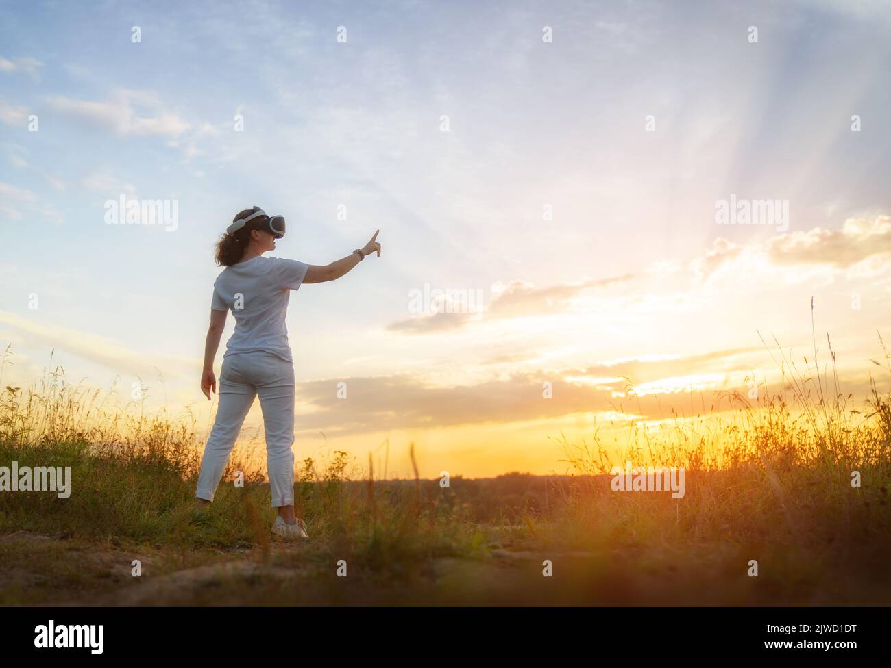 Metaverse technology concept. Woman with VR virtual reality goggles standing on nature. Futuristic lifestyle. Stock Photo