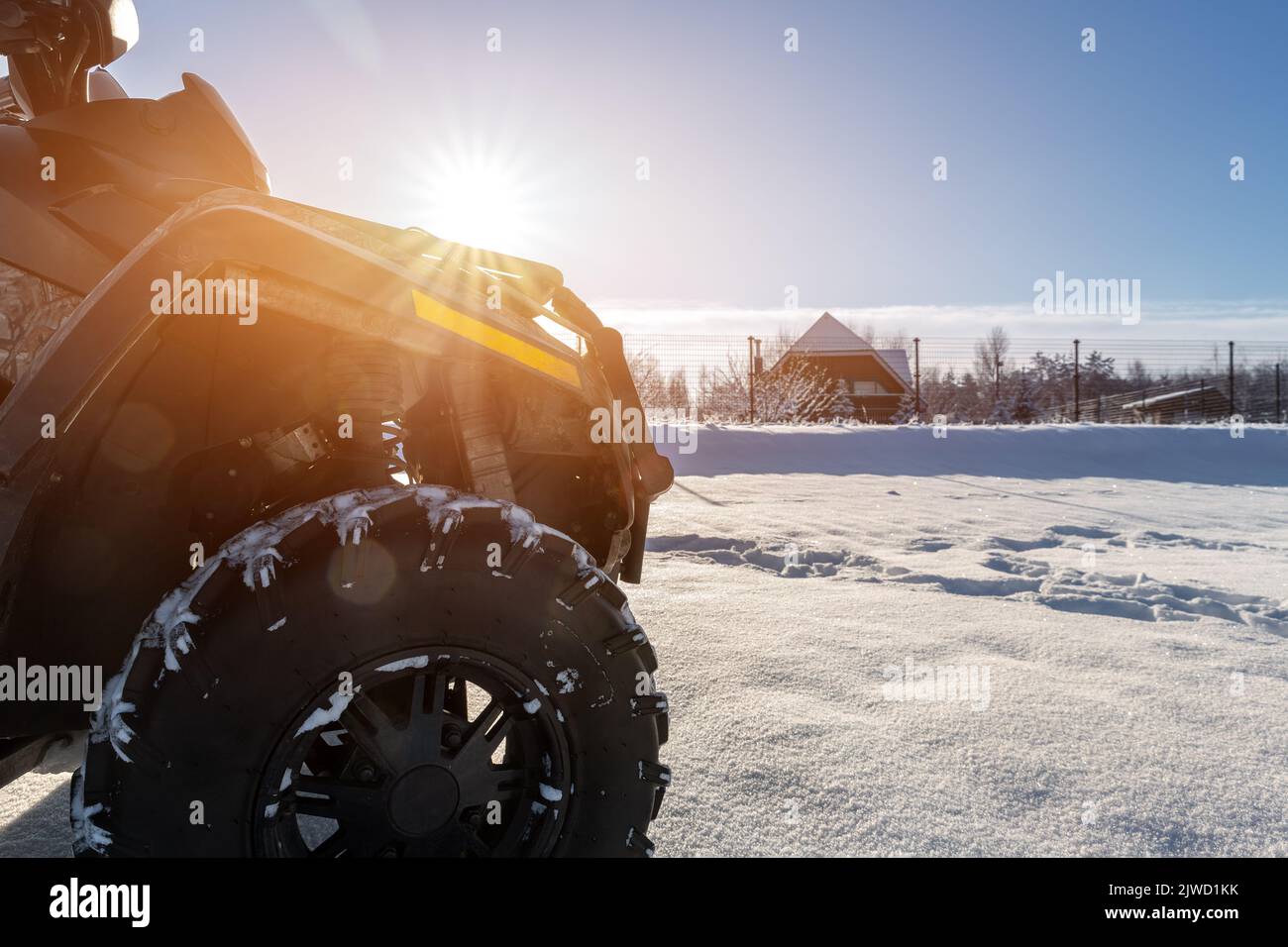 Side POV close-up detail view of quad bike offroad vehicle parked in snowdrift track on sunny snowy cold winter morning against clear blue sky. ATV Stock Photo