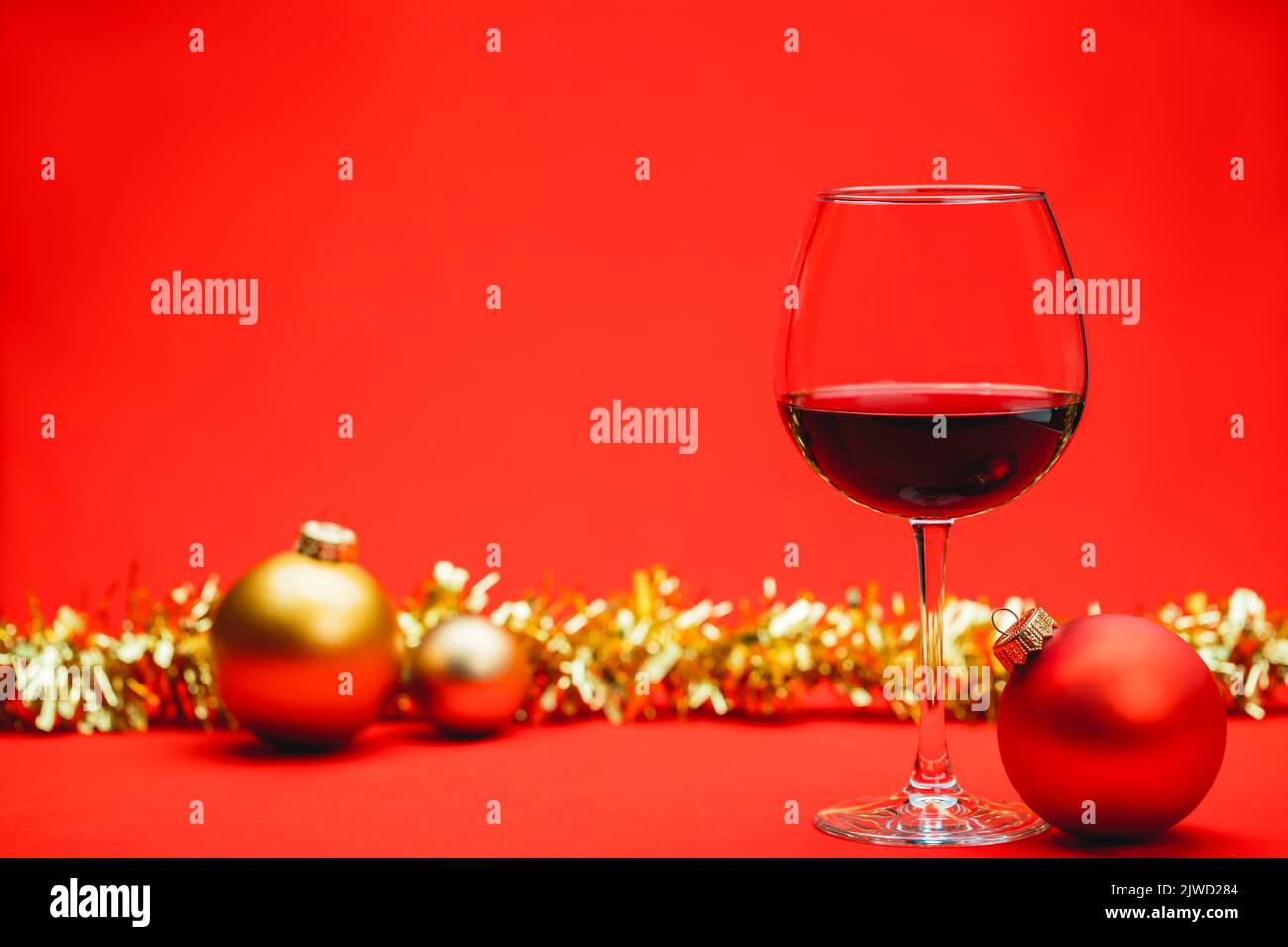 Glass of red wine with christmas baubles and tinsel on red background - christmas drink concept Stock Photo