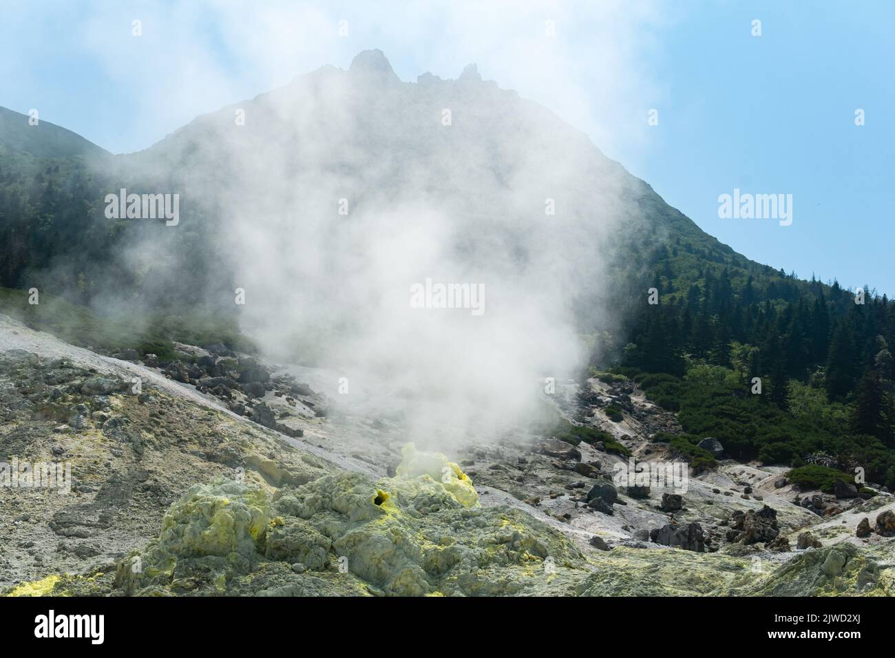 bright smoking fumarole with sulfur deposits against the background of the Mendeleev volcano peak on the island of Kunashir Stock Photo