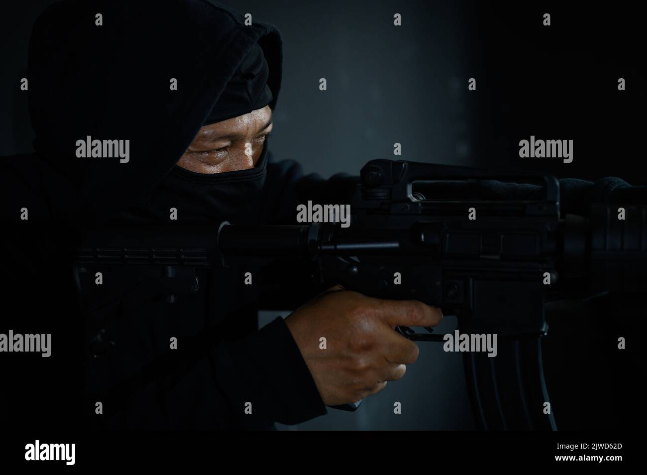 Side view of terrorist in black balaclava mask aiming with machine gun Stock Photo