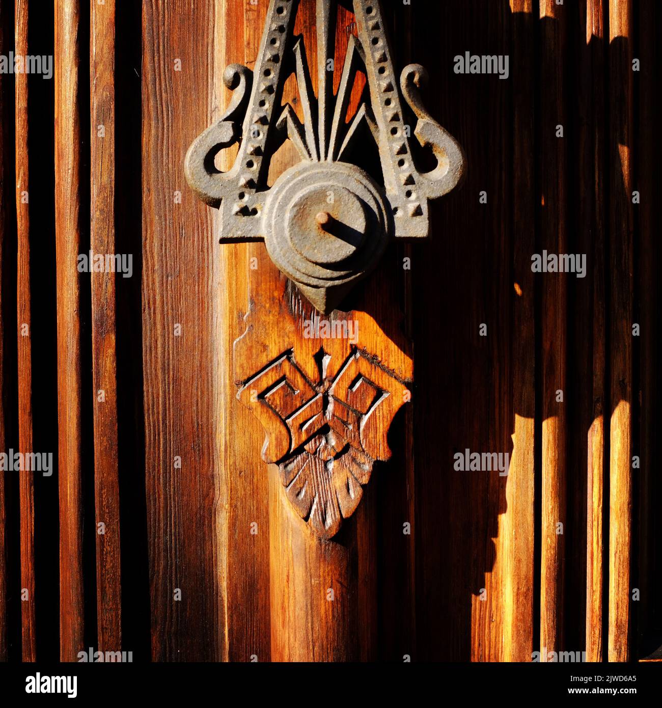 Brass door knocker on wooden door with strong shadows cast by afternoon sunlight Stock Photo