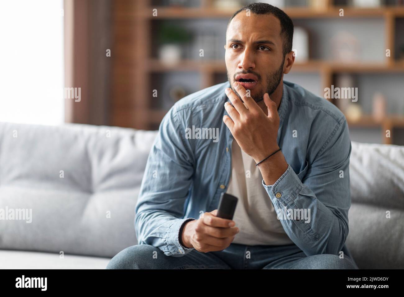 Shocked Black Man With Remote Controller In Hand Sitting On Couch Stock Photo