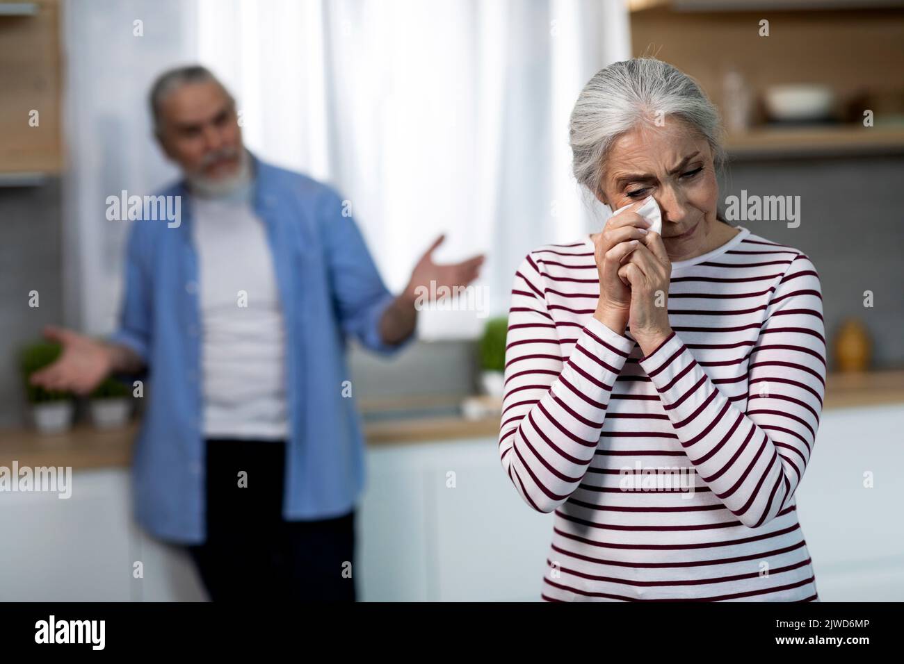 Depressed Senior Woman Crying In Kitchen During Argue With Husband Stock Photo
