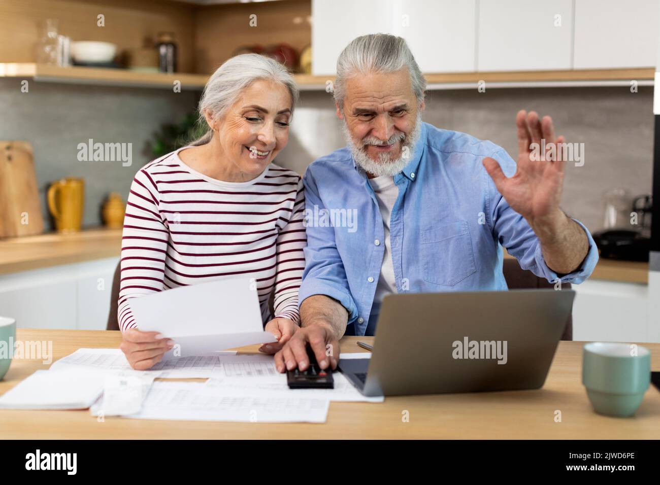 Senior Spouses Making Video Call With Accountant While using Laptop In Kitchen Stock Photo