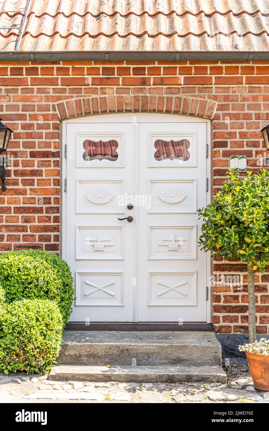 White front door with small square decorative windows and flower pots