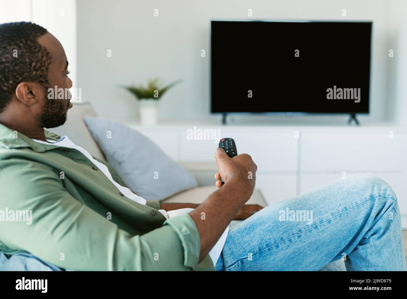 Black man watching tv, looking at black blank television monitor for