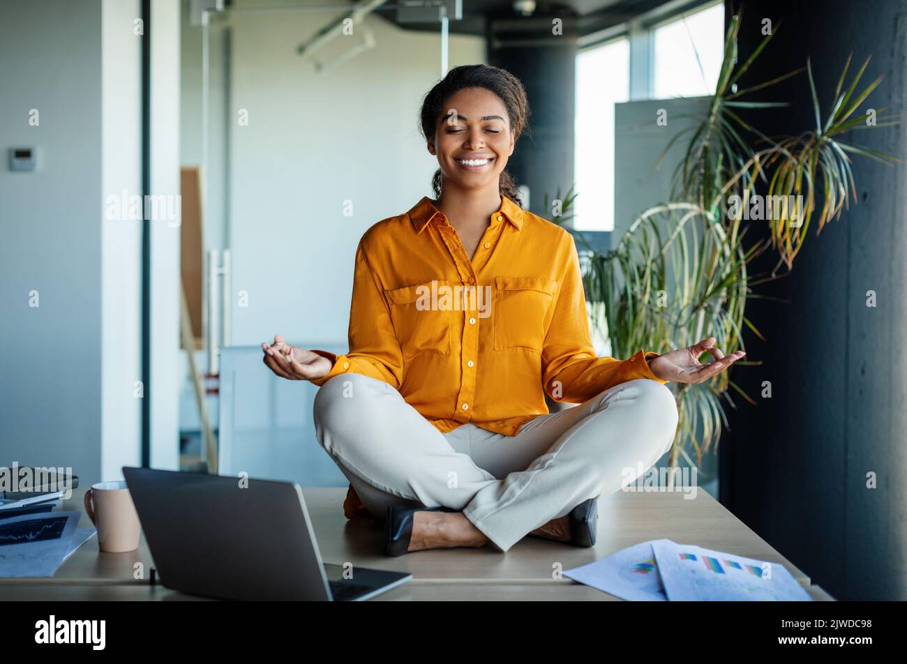 Office zen. Calm black businesswoman meditating with closed eyes on ...