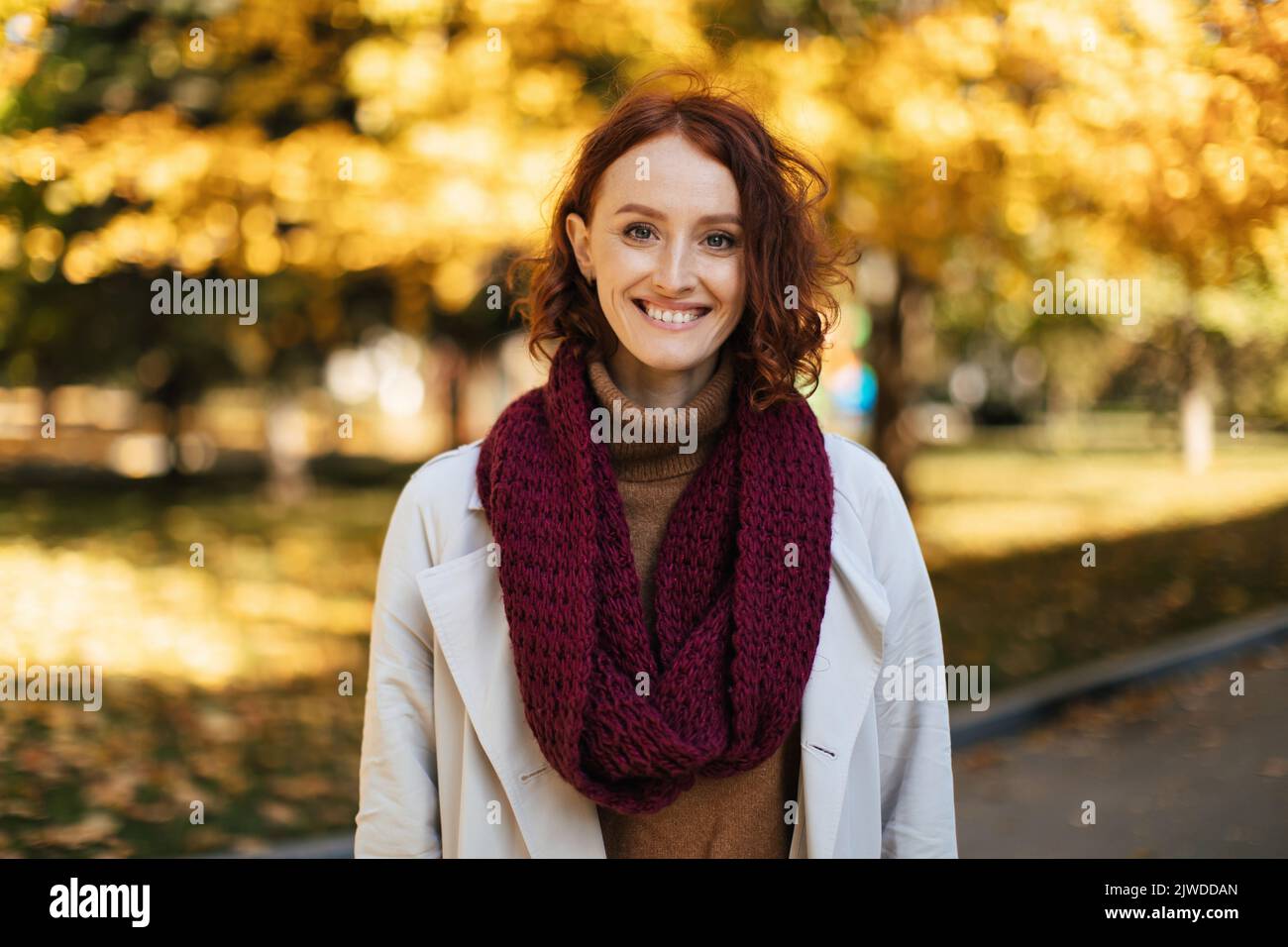 Happy redhead millennial european woman in raincoat with scarf enjoy great weather, free time in city park Stock Photo