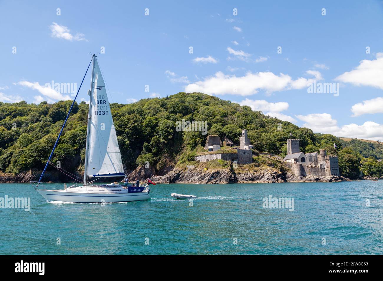 A yacht with it's sail up sailing past Dartmouth Castle & St Petroc's Church at the mouth of Dartmouth harbour Stock Photo