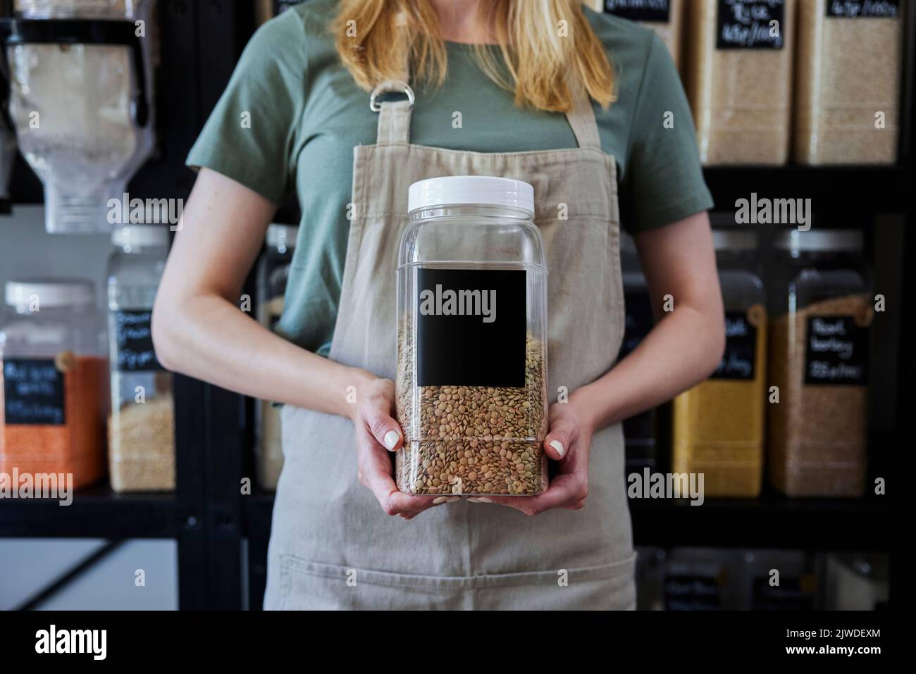 Close Up Of Sales Assistant In Sustainable Plastic Free Wholefood Store Holding Container With Blank Label Stock Photo