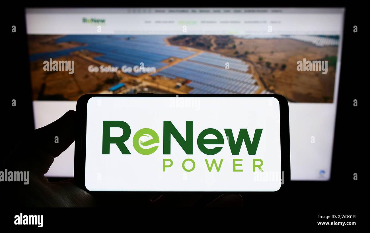 Person holding smartphone with logo of Indian company ReNew Energy Global plc on screen in front of website. Focus on phone display. Stock Photo