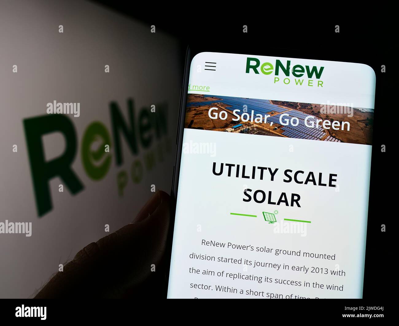 Person holding cellphone with website of Indian company ReNew Energy Global plc on screen in front of logo. Focus on center of phone display. Stock Photo