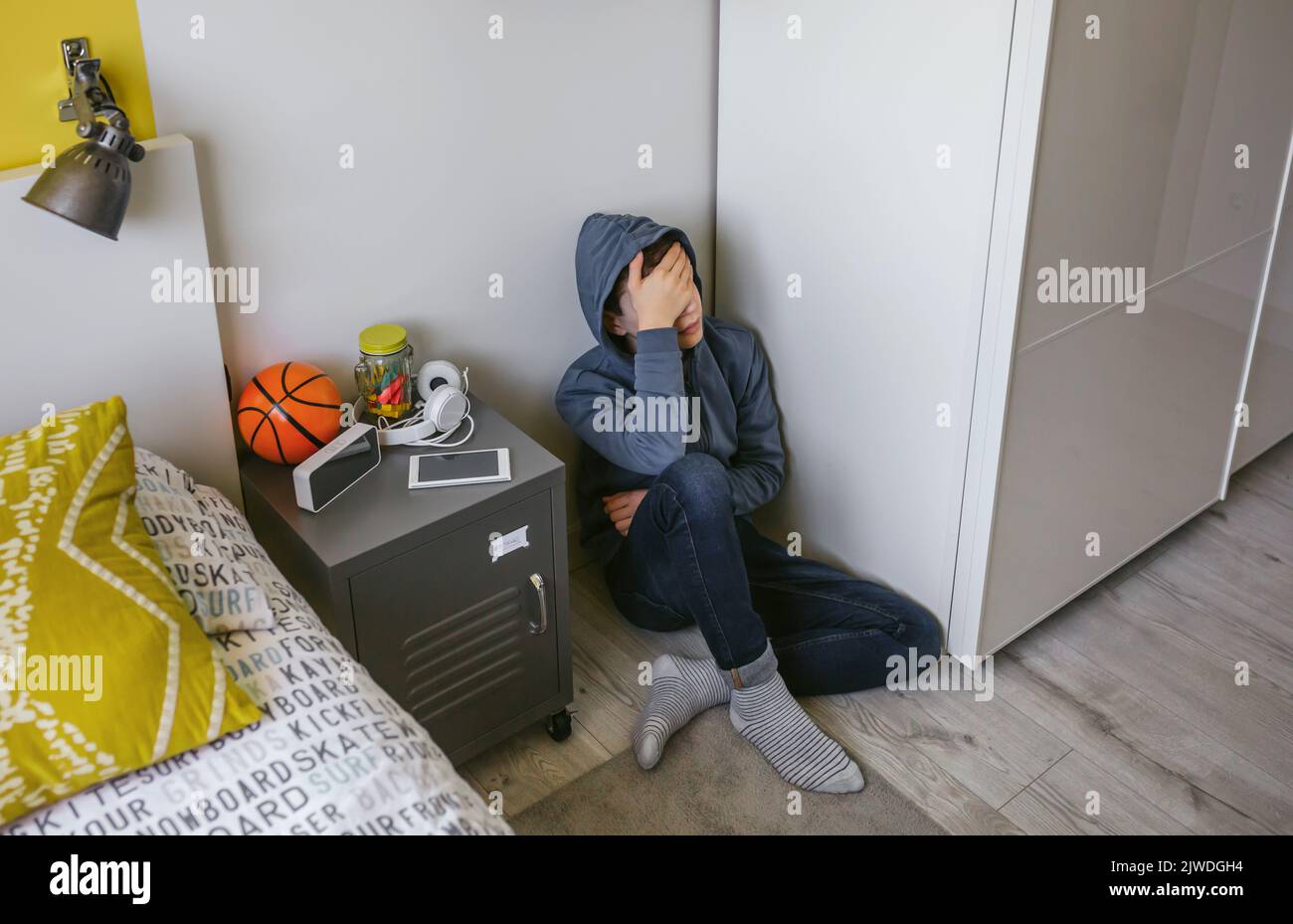 Depressed male teenager sitting on the floor in his bedroom Stock Photo