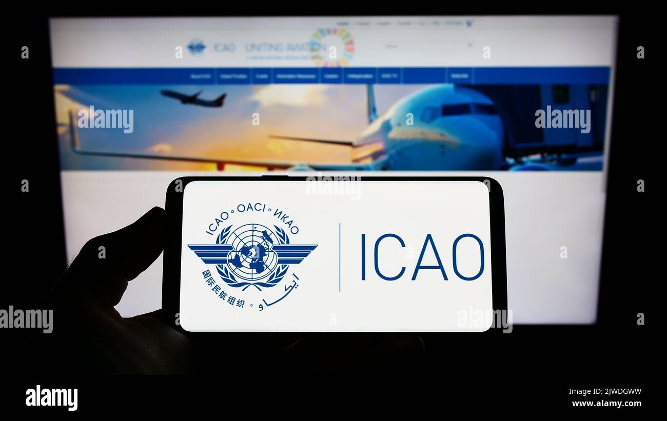 Person holding smartphone with logo of International Civil Aviation Organization (ICAO) on screen in front of website. Focus on phone display. Stock Photo