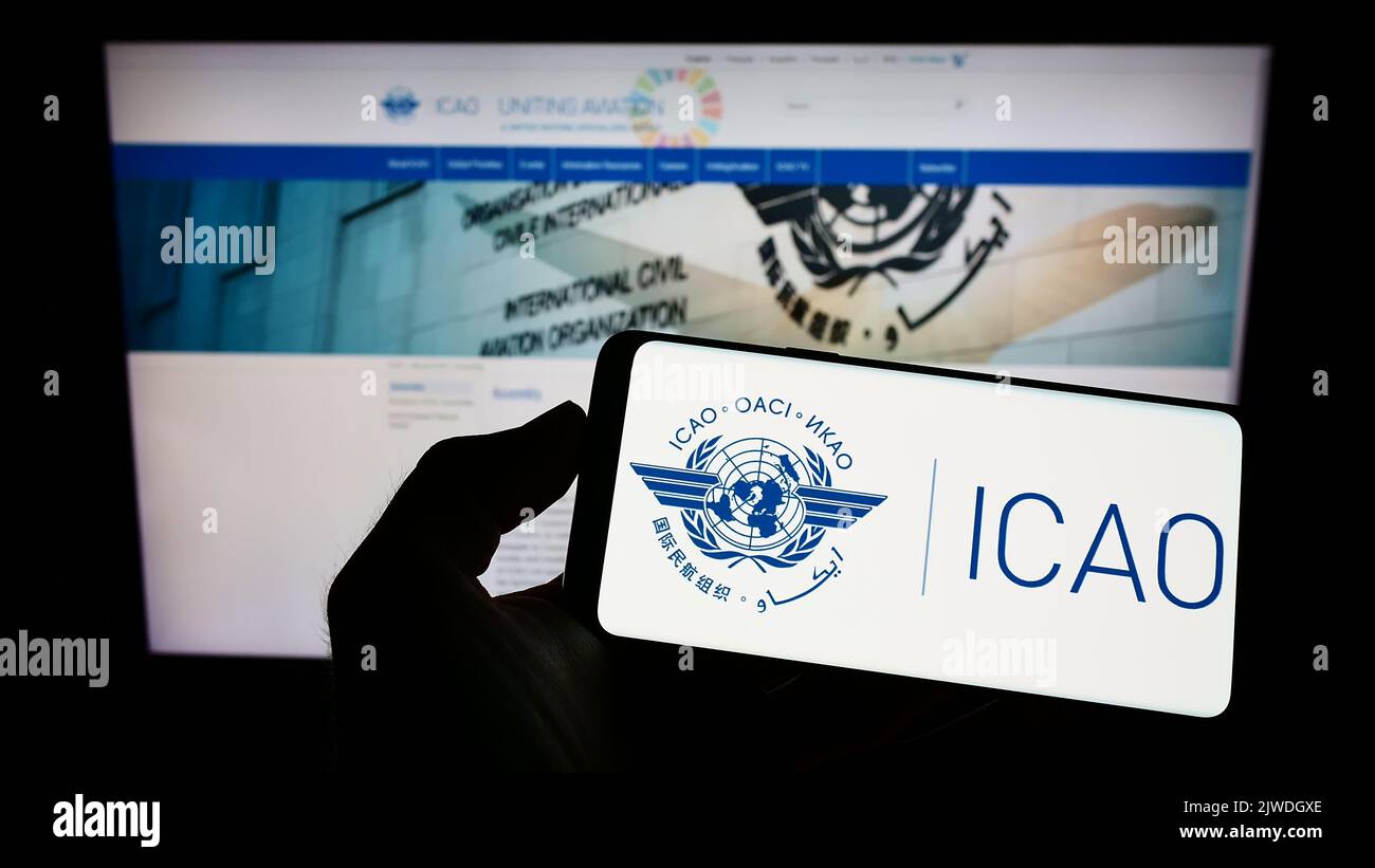 Person holding cellphone with logo of International Civil Aviation Organization (ICAO) on screen in front of webpage. Focus on phone display. Stock Photo
