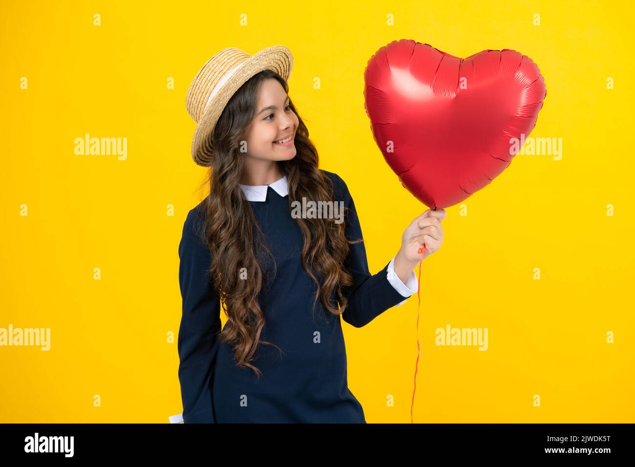 Cheerful lovely romantic teen girl hold red heart balloon, symbol of love for valentines day isolated on yellow background. Stock Photo