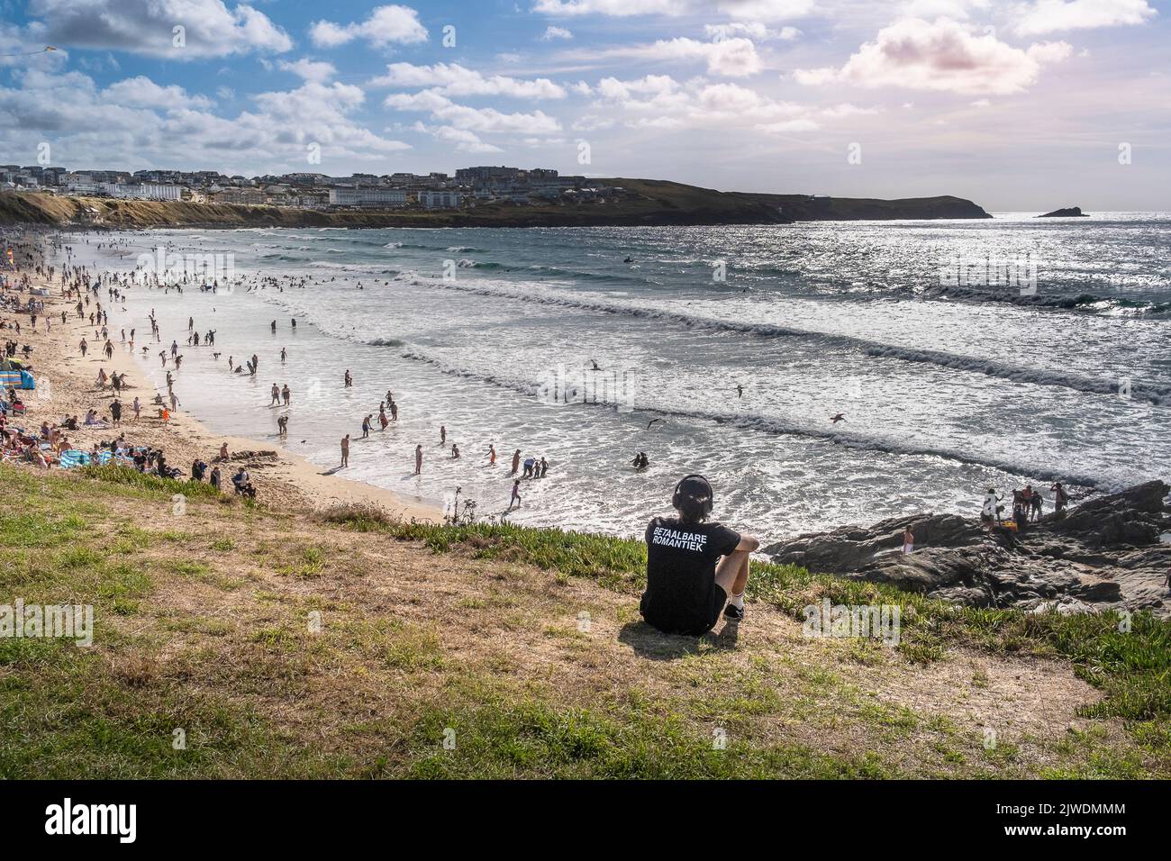 A man sitting on the headland overlooking holidaymakers on a busy Fistral Beach in Newquay in Cornwall in the UK. Stock Photo