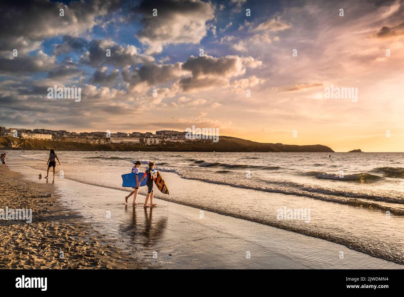 Two young boys carrying their body boards boogie boards and walking into the sea at Fistral in golden light in the evening in Newquay in Cornwall in t Stock Photo
