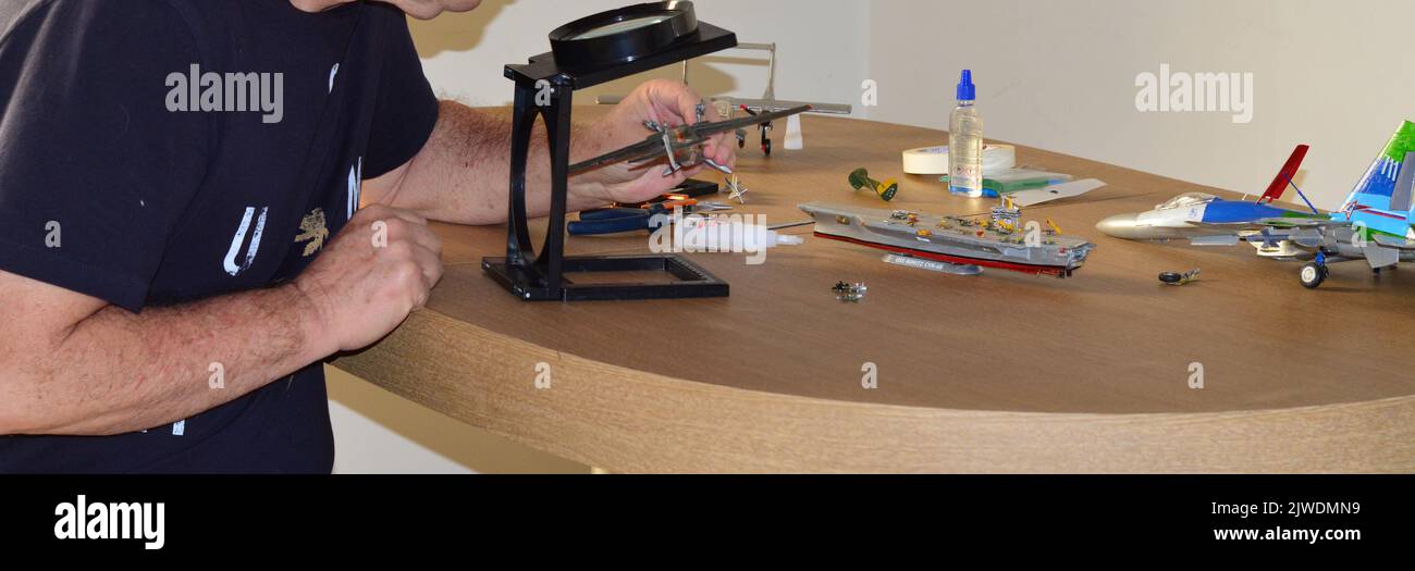 Plastic model kit, man assembling kit, with magnifying glass, selective focus, intentional cropping Stock Photo