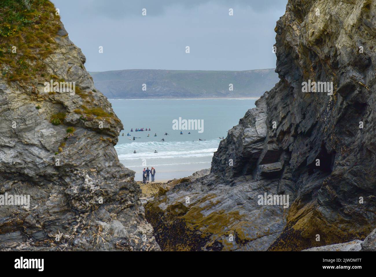 A distant view through a gap in the cliffs of surfers in the sea at Great Western Beach in Newquay in Cornwall in the UK. Stock Photo