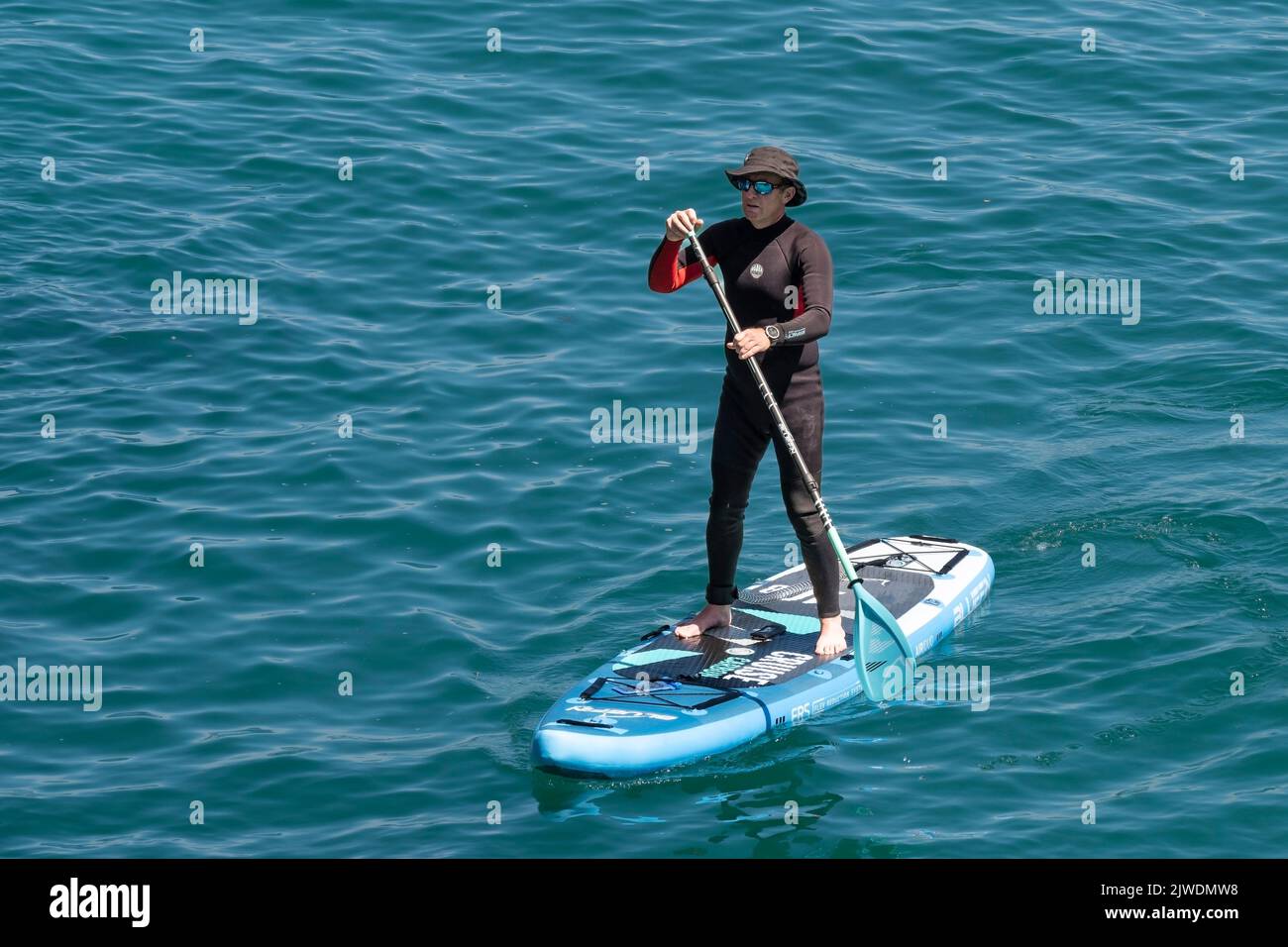A holidaymaker standing on a Stand Up Paddleboard In Newquay Bay in Cornwall in England in the UK. Stock Photo