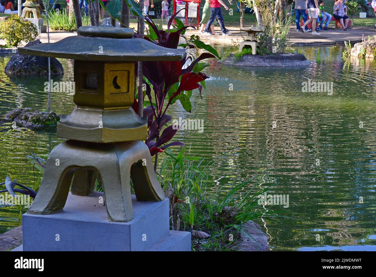 Stone lantern in Japanese garden at cherry blossom festival in the countryside of Brazil, in the background tourists visiting the place Stock Photo