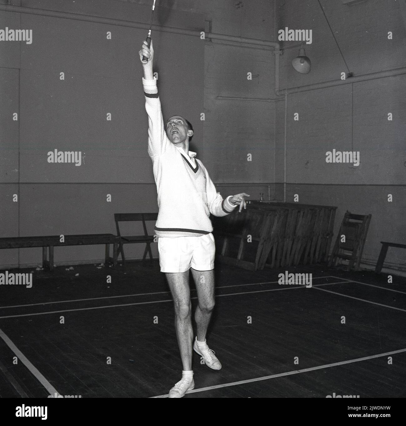 1965, historical, English male badminton player on court, stretching high to play a shot, Scotland, UK, wearing al v-neck sweater, shorts and traditional plimsolls. Stock Photo