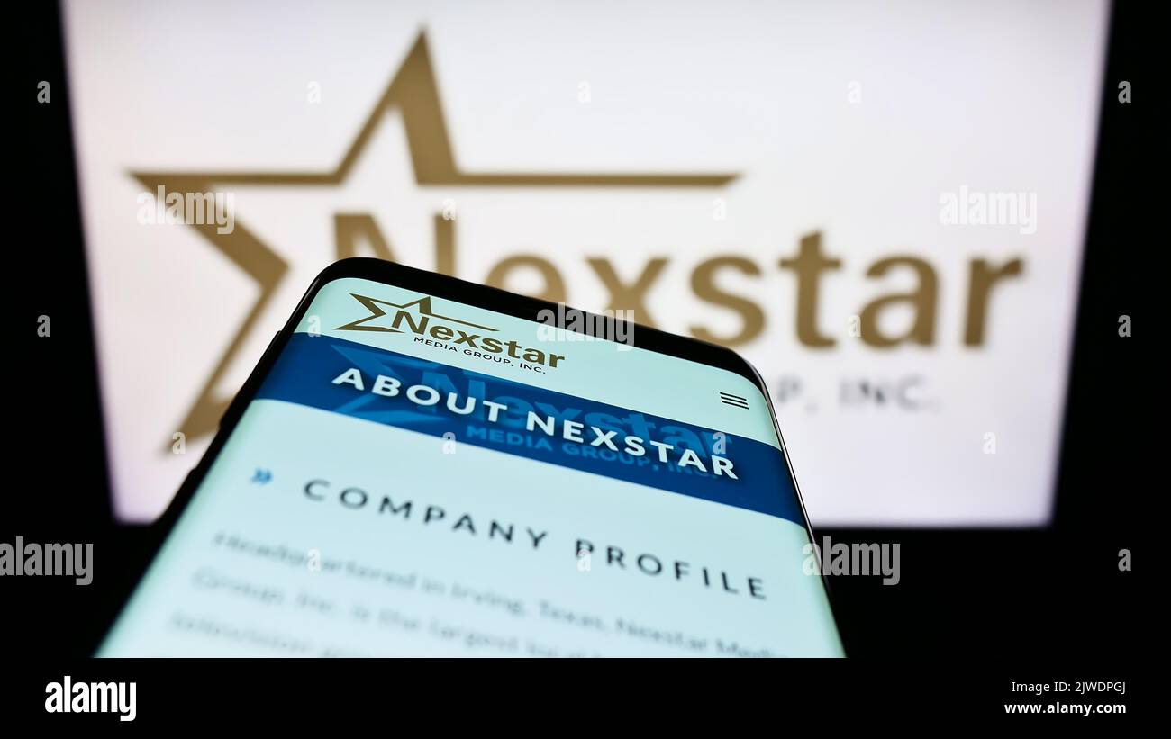 Mobile phone with webpage of American television company Nexstar Media Group Inc. on screen in front of logo. Focus on top-left of phone display. Stock Photo