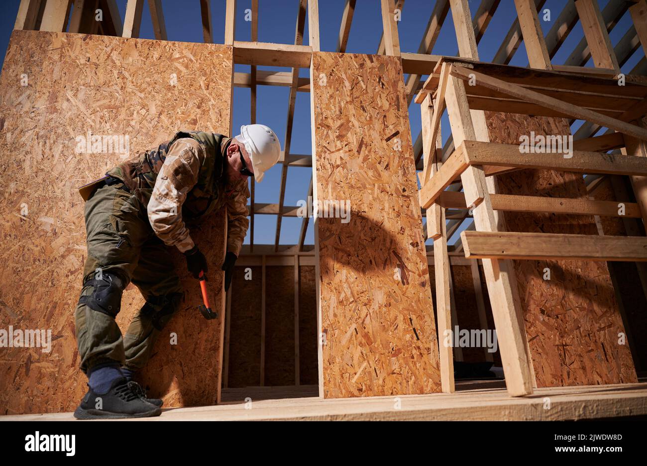 Carpenter hammering nail into OSB panel on the wall of future cottage