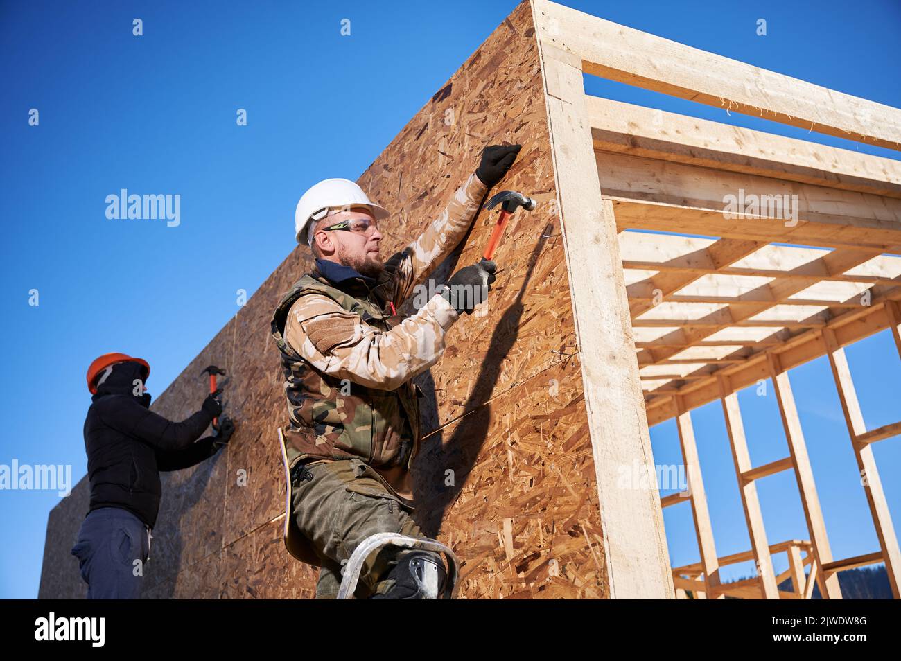 Carpenters hammering nail into OSB panel on the wall of future cottage