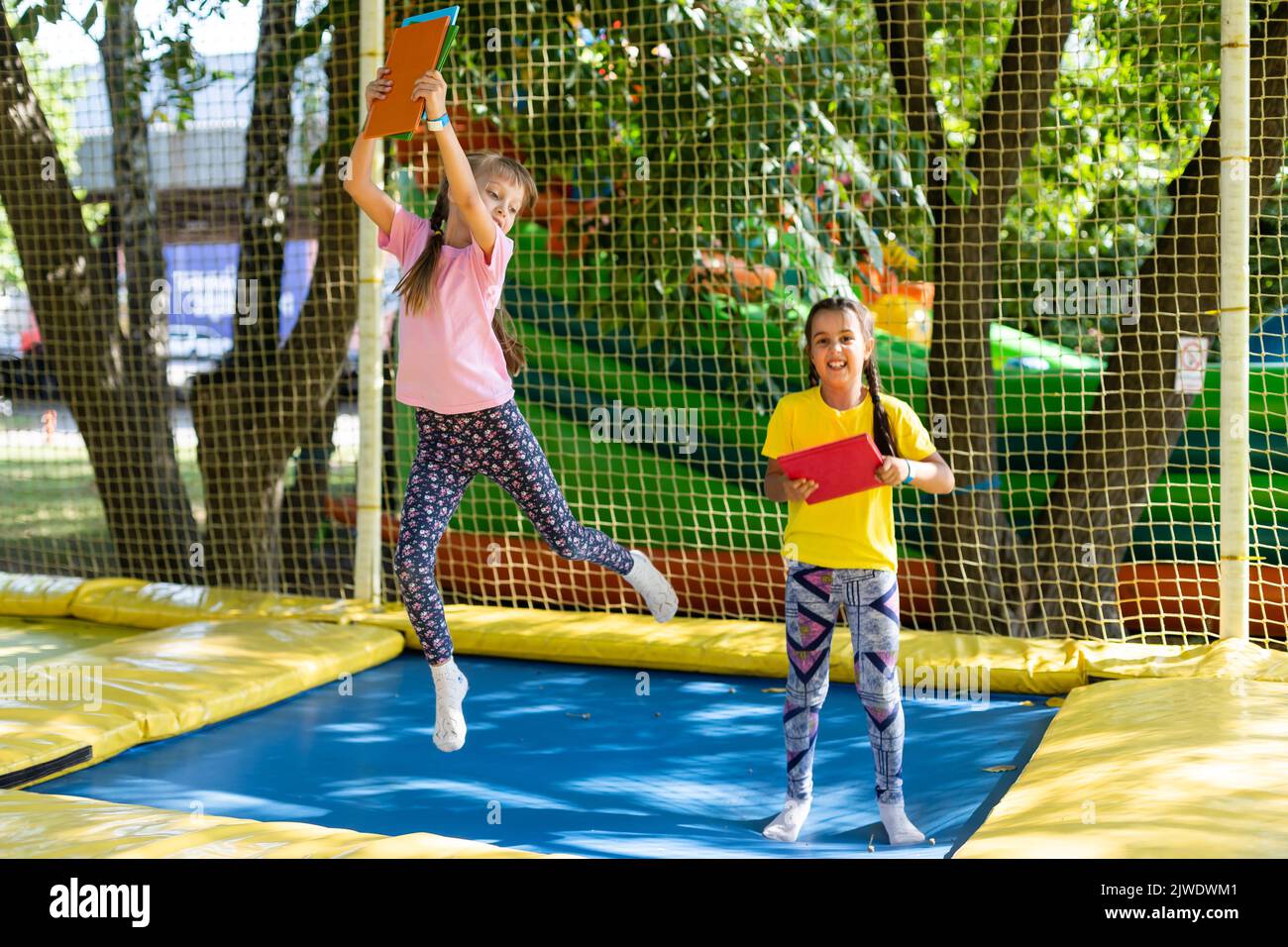 Two little girls in the summer jump on a trampoline, smiling and ...