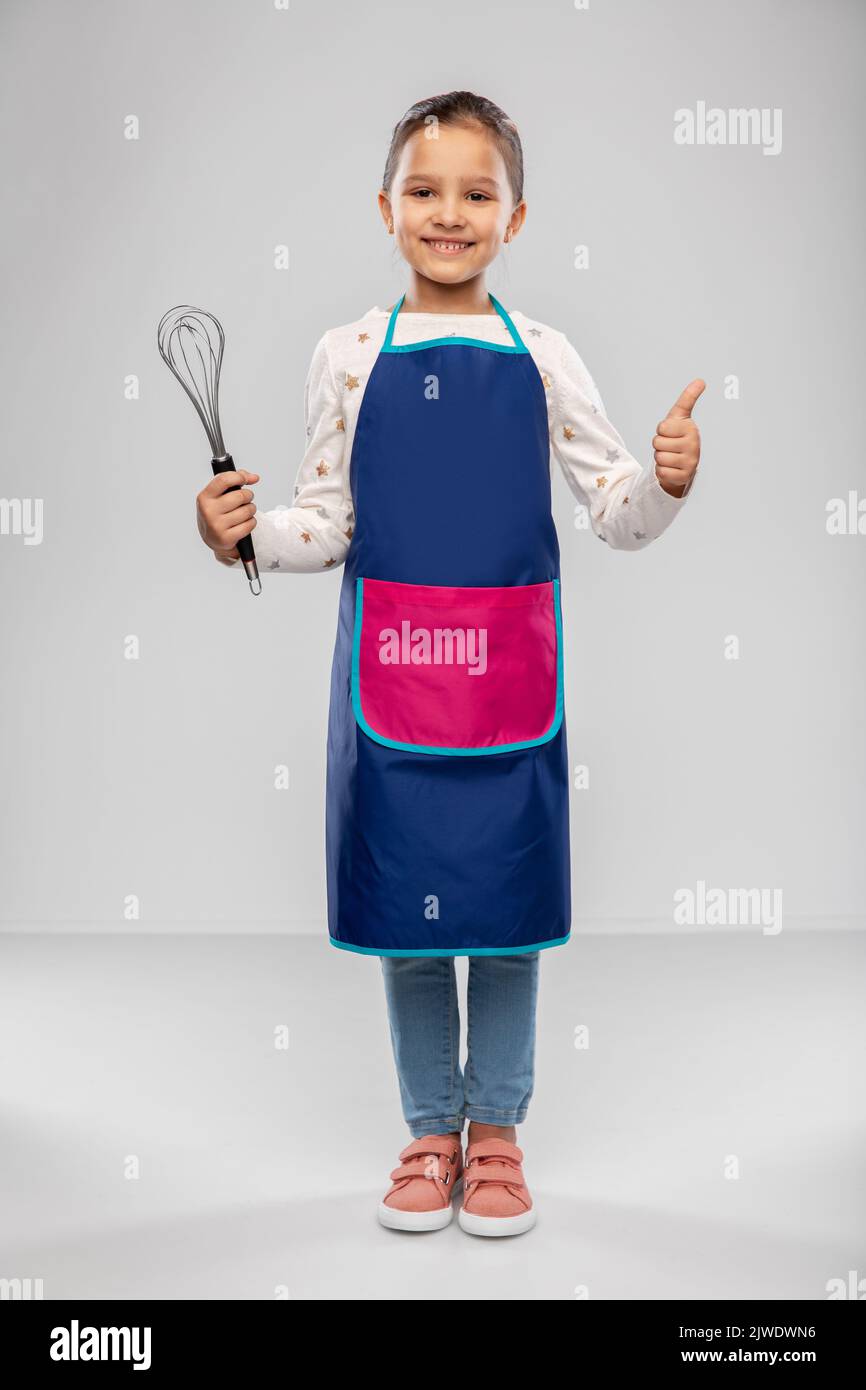 little girl in apron with whisk showing thumbs up Stock Photo