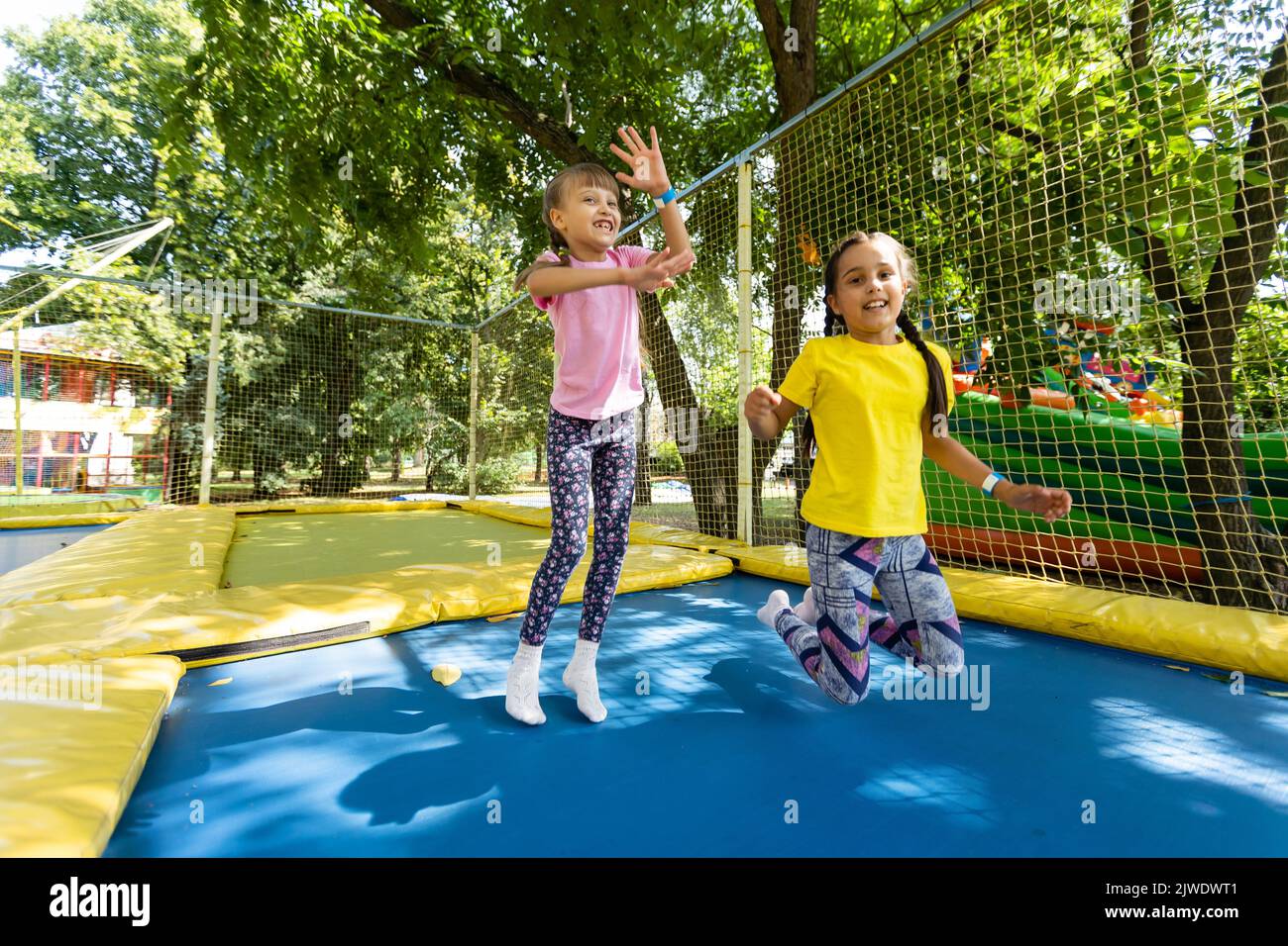Two little girls in the summer jump on a trampoline, smiling and ...