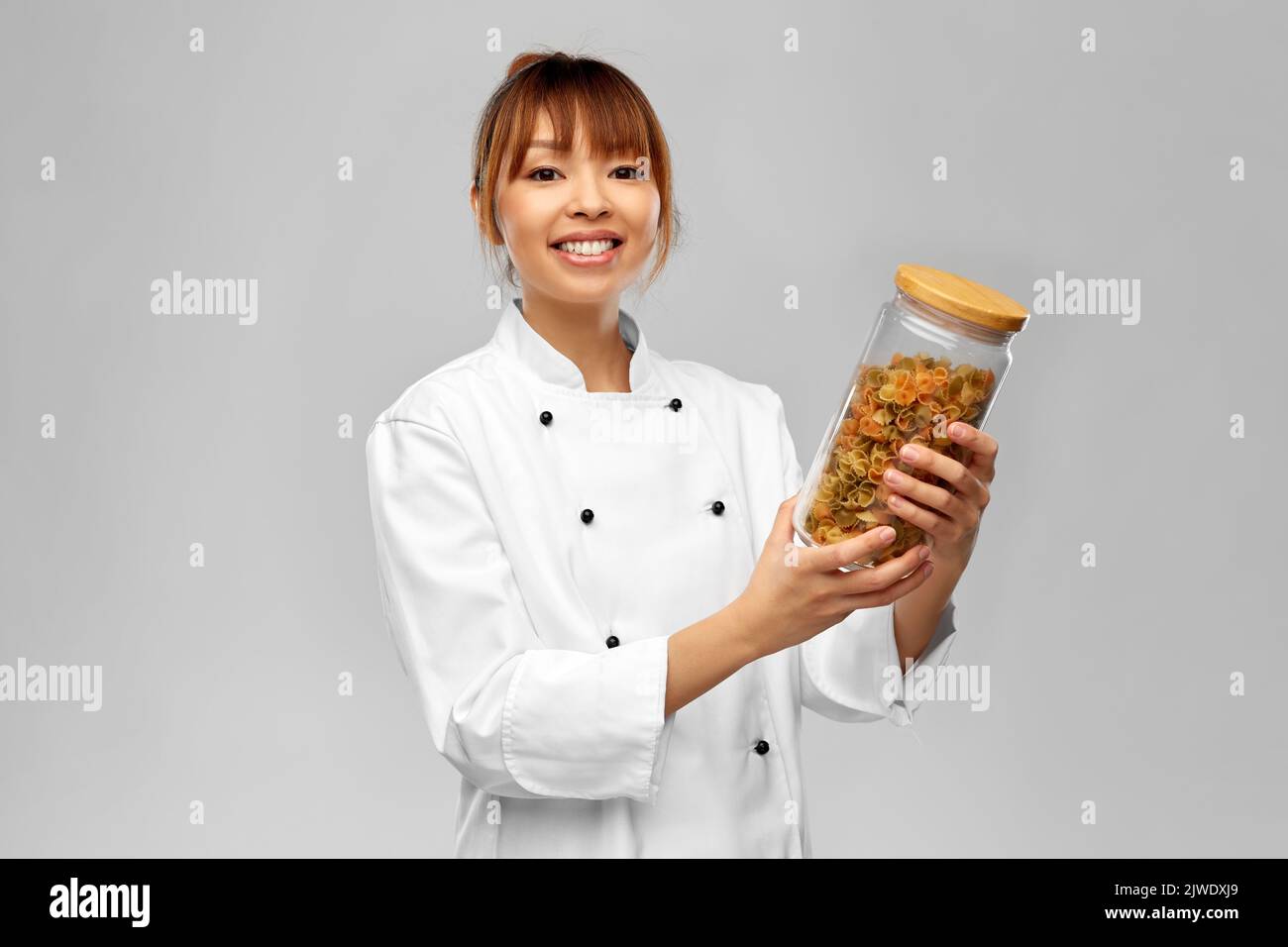 smiling female chef holding jar with pasta Stock Photo