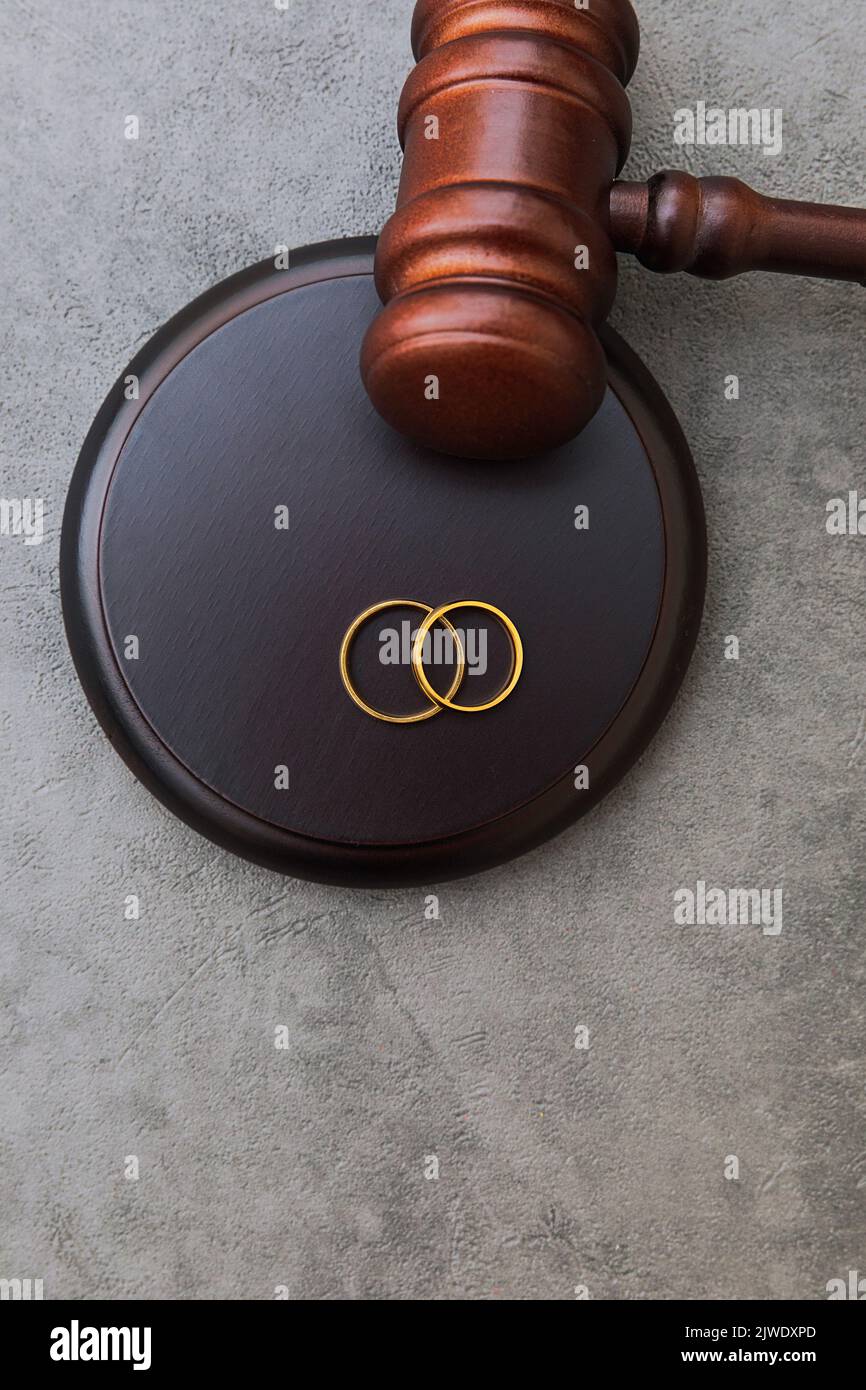 Law theme. Judge gavel wedding rings on concrete stone grey background